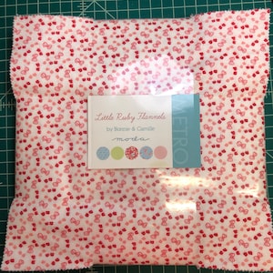 May include: A white fabric with a red and pink bow pattern. The fabric is packaged with a label that reads "Little Ruby Flannels by Bonnie & Camille" and a Moda logo.