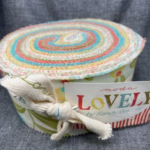 Peut inclure: Un rouleau de tissu avec un motif floral dans des tons de vert, jaune et rose. Le tissu est enroulé et noué avec un ruban blanc. L'étiquette indique "moda LOVELY by Sandy Gervais".