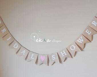 May include: A burlap banner with the words "Bridal Shower" in white letters. A pink heart is between the words "Bridal" and "Shower".