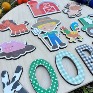 Pu&ograve; includere: Un puzzle in legno a tema fattoria con ritagli colorati di animali e personaggi della fattoria. Il puzzle include un fienile rosso, un cavallo marrone, un maiale rosa, un contadino, una mucca, un gallo e un trattore verde. Sono incluse anche le lettere "KOOP".