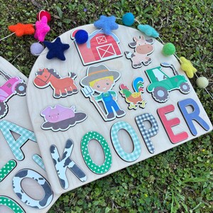 Pu&ograve; includere: Puzzle in legno a tema fattoria con ritagli colorati di animali e oggetti della fattoria. Il puzzle include un trattore, un maiale, un cavallo, una mucca, un contadino e un gallo. Il nome "KOOPER" &egrave; scritto con singole lettere.