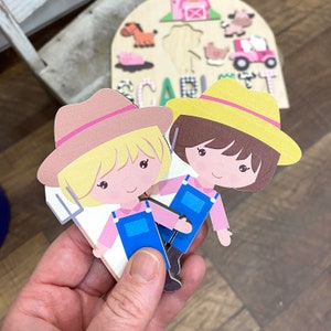 Pu&ograve; includere: Due ritagli di carta di contadini dei cartoni animati, uno biondo e uno bruno, con camicie rosa, tute blu e cappelli di paglia. La contadina bionda tiene un forcone. Un puzzle in legno a tema fattoria &egrave; sullo sfondo.