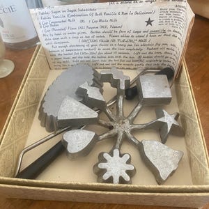 May include: A vintage rosette iron set with various shapes, including stars, bells, and snowflakes, in a decorative box. The set includes a handle and instructions. The metal molds are silver-colored.