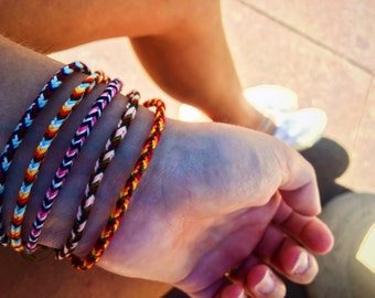 Puede incluir: Una muñeca adornada con varios brazaletes de amistad de colores. Los brazaletes están hechos de cuerda trenzada en varios tonos de rojo, azul, amarillo, blanco y negro.