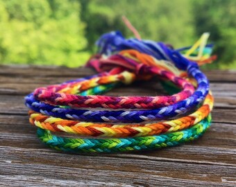 Puede incluir: Cuatro pulseras de amistad coloridas con un patrón de arcoíris. Las pulseras están hechas de cuerda trenzada y tienen borlas en los extremos.