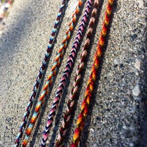 Puede incluir: Cinco pulseras de amistad coloridas hechas con hilo trenzado. Las pulseras son en tonos de rojo, naranja, amarillo, azul, verde, blanco y negro.