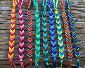 Puede incluir: Una colección de pulseras de amistad de chevron de colores con varias combinaciones de colores, incluyendo rojo, rosa, amarillo, verde, azul y naranja.