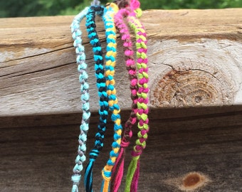 Puede incluir: Seis pulseras de amistad coloridas hechas con cuerda trenzada en tonos de azul, verde, rosa, amarillo, negro y gris.