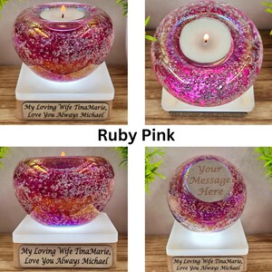 May include: Ruby pink glass candle holder with a lit candle, set on a white base. The base has text that reads "My Loving Wife TinaMarie, Love You Always Michael". The candle holder is a decorative item.