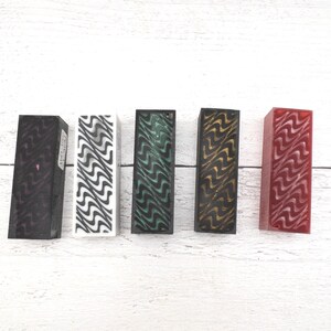 May include: Five rectangular blocks with wavy patterns in various colors: black with purple, white with black, green with black, black with gold, and red with white. The blocks are arranged in a row.