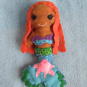 May include: A handmade felt mermaid doll with orange hair, a purple and blue top, and a green and blue tail with a pink starfish.