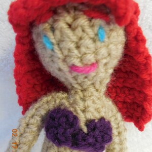 May include: Crocheted doll with red hair, a purple top, and blue eyes.