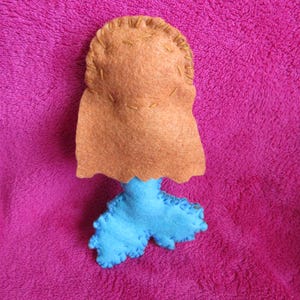 May include: A felt mermaid doll with a brown head and blue tail. The doll is handmade and has a simple design.