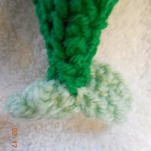 May include: A green crocheted Christmas tree ornament with a white crocheted base.