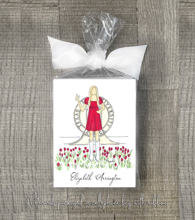 May include: A set of notecards featuring a hand-drawn illustration of a woman in a red dress standing in front of the University of Texas at Austin seal. The notecards are packaged in a cellophane bag with a ribbon and the name "Elizabeth Arrington" is printed below the illustration.