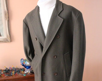 May include: A long, dark green double-breasted wool coat with a white turtleneck sweater underneath. The coat has four buttons down the front and two pockets on the sides.