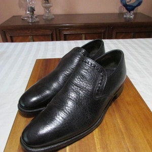 May include: A pair of black leather slip-on shoes with a braided detail on the side.