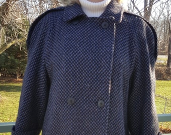 May include: A long, double-breasted coat with a herringbone pattern in shades of gray and black. The coat has a collar and long sleeves with buttoned cuffs.