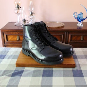 May include: A pair of black leather ankle boots featuring a smooth finish, rounded toes, and black laces threaded through metal eyelets. The boots have a sturdy black rubber sole and a high-top design that reaches above the ankle for support.