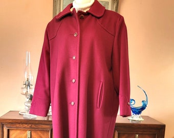 May include: A long, burgundy wool coat with a button-up front and a single pocket on the left side. The coat has a classic, tailored look.