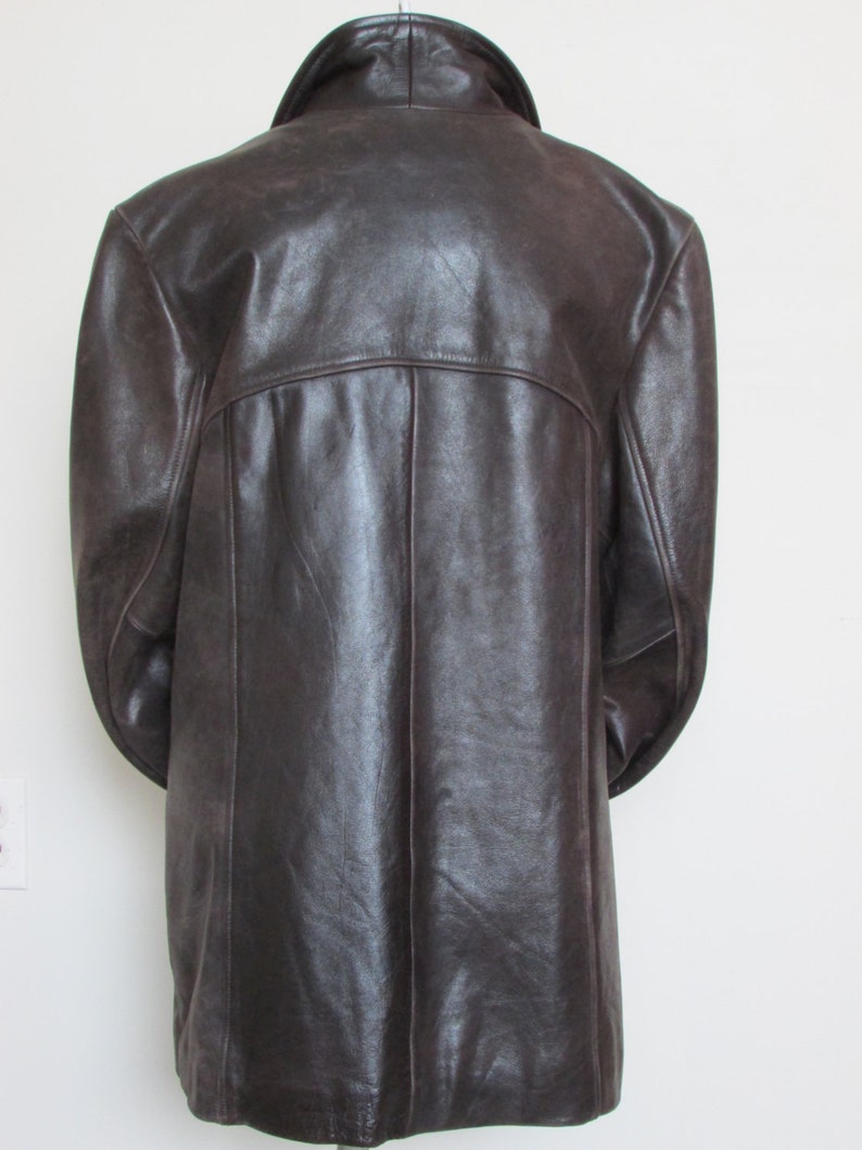 May include: A brown leather jacket with a long cut and a collar. The jacket has a zipper closure and two pockets on the front.