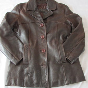 May include: A brown leather jacket with a button closure and a collar. The jacket has a label that says "SAHAR" on it.