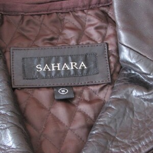 May include: A brown leather jacket with a quilted lining and a label that reads "SAHARA" with a size "M" tag.