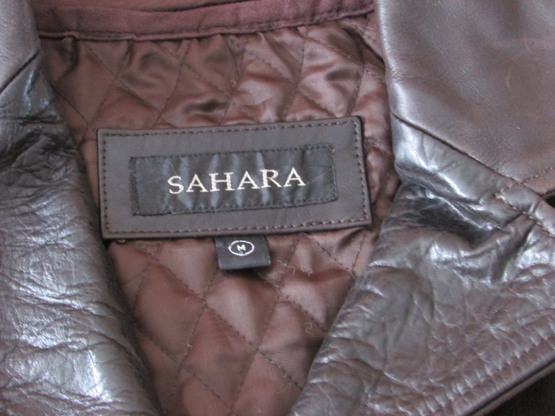 May include: A brown leather jacket with a quilted lining and a label that reads "SAHARA" with a size "M" tag.