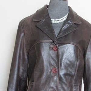 May include: A brown leather jacket with a button closure and a collar. The jacket has a slightly fitted silhouette.
