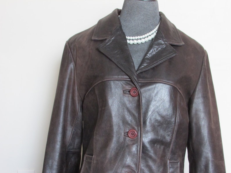 May include: A brown leather jacket with a button closure and a collar. The jacket has a slightly fitted silhouette.