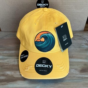 May include: Yellow baseball cap with a distressed brim, featuring a circular graphic of a sunset over ocean waves. The cap has the "DECKY" logo and "LOW CROWN" and "ORIGINAL" labels.