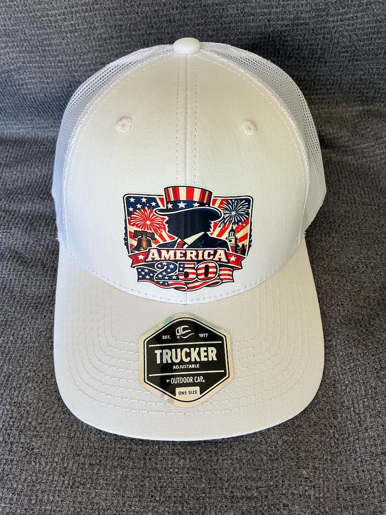 Peut inclure: Une casquette trucker blanche avec un dos en filet et un motif sur le devant repr&eacute;sentant l'Oncle Sam, la Liberty Bell, des feux d'artifice et le texte AMERICA 250. Un autocollant noir et argent sur la visi&egrave;re indique TRUCKER ADJUSTABLE BY OUTDOOR CAP ONE SIZE.