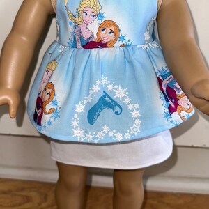 May include: A blue sleeveless dress with a white underskirt. The dress features a pattern of snowflakes and the characters Elsa and Anna from the movie Frozen.
