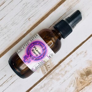 Puede incluir: Una botella de vidrio marr&oacute;n con un pulverizador negro. La etiqueta es morada y blanca y dice "Hot Flash Relief", "Flash Ease", "Cooling Body Mist" y "60ml/2oz".