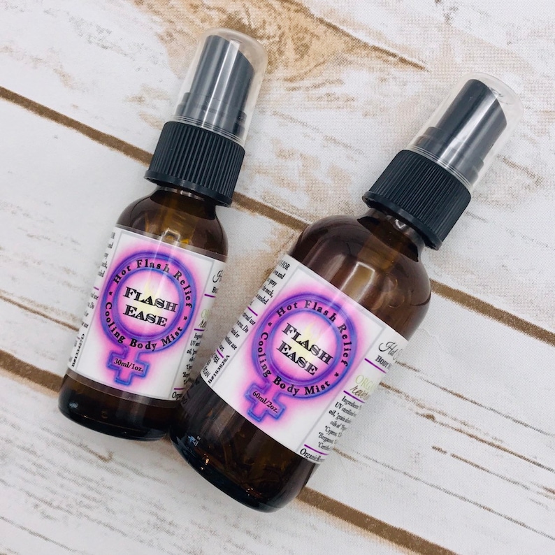 Puede incluir: Dos botellas de vidrio &aacute;mbar con pulverizadores negros y etiquetas que dicen "Hot Flash Relief" y "Flash Ease Cooling Body Mist". Las botellas est&aacute;n sobre una superficie de madera blanca.