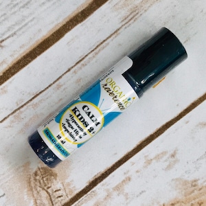 May include: A blue and white roll-on bottle labeled "CALM KIDS 2+" with the text "Hyperactivity, Sugar Highs, Impulsivity" and "ORGANIC reverence" on the label. The bottle contains 10 ml of aromatherapy oil.