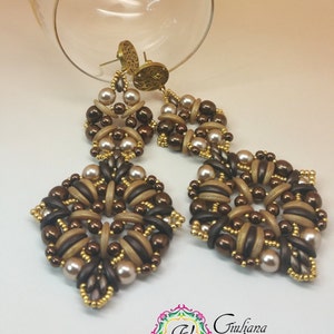 May include: A pair of long, brown and beige beaded earrings with gold accents. The earrings are in the shape of a flower with a center of brown beads and a ring of beige beads. The earrings are hanging from gold hooks.