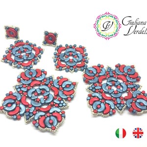 Op de afbeelding: Een paar oorbellen met een geometrisch ontwerp in rood en blauw. De oorbellen zijn gemaakt van kleine kralen en hebben de vorm van bloemen. De oorbellen hangen aan een zilveren haak.