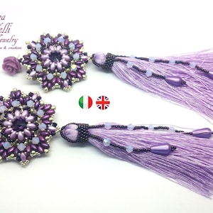 Puede incluir: Un par de pendientes de cuentas moradas y plateadas con borla. Los pendientes tienen un diseño floral y están adornados con pequeñas cuentas moradas.