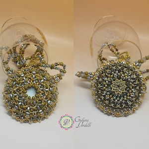 May include: A gold and silver beaded necklace with a large round pendant. The pendant is made of small beads in a circular pattern. The necklace is displayed on a glass surface.