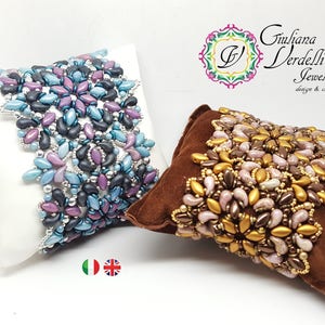 Può includere: Due braccialetti di perline su cuscini di velluto bianco e marrone. Il braccialetto a sinistra è realizzato con perline blu, viola e nere. Il braccialetto a destra è realizzato con perline dorate, marroni e rosa. Entrambi i braccialetti sono realizzati con perline a seme e presentano un design floreale.