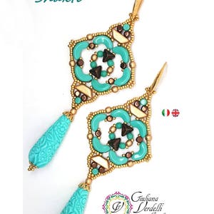 Könnte beinhalten: Türkisfarbene und goldene Perlenohrringe mit geometrischem Design und einem tropfenförmigen türkisfarbenen Anhänger. Die Ohrringe sind mit "Shakti" und "Giuliana Verdelli Jewelry design & creations" beschriftet.