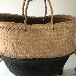 May include: A large woven basket with a black bottom and rope handles. The basket is made of natural materials and has a rustic look.