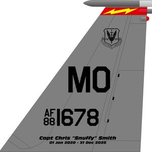 May include: A gray aircraft vertical stabilizer featuring a black Air Combat Command emblem, the letters MO, and the serial number AF 88 1678. A red stripe with a yellow lightning bolt sits near the top, with text reading Capt Chris Snuffy Smith 01 Jan 2020 - 31 Dec 2026.