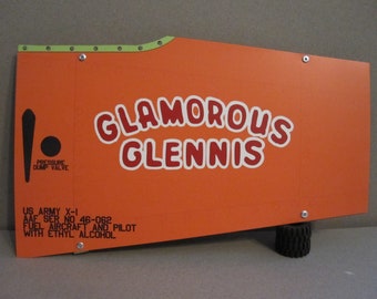 May include: Orange and white airplane tail section with the text "Glamorous Glennis" and "US Army X-1 AAF Ser No 46-062 Fuel Aircraft and Pilot with Ethyl Alcohol".