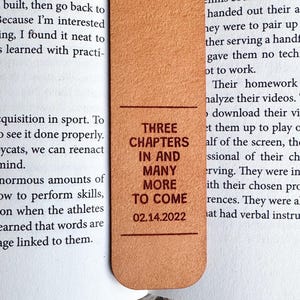 May include: A brown leather bookmark with the text "THREE CHAPTERS IN AND MANY MORE TO COME 02.14.2022" printed in red.