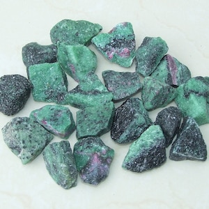 May include: A collection of green and black rough gemstones. The stones are various sizes and shapes.