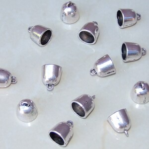 May include: A group of 12 silver metal end caps for jewelry making. The end caps have a rounded top and a small loop on the side.