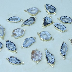 May include: A collection of 17 agate slices with gold-toned metal accents. The agate slices are a mix of white and black with a natural crystal pattern. The slices are oval-shaped and have a hole on each side for attaching to jewelry or other crafts.