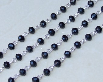 Op de afbeelding: Een streng zwarte facetgeslepen kralen geregen aan een zilveren ketting. De kralen zijn gelijkmatig verdeeld en de ketting is delicaat.